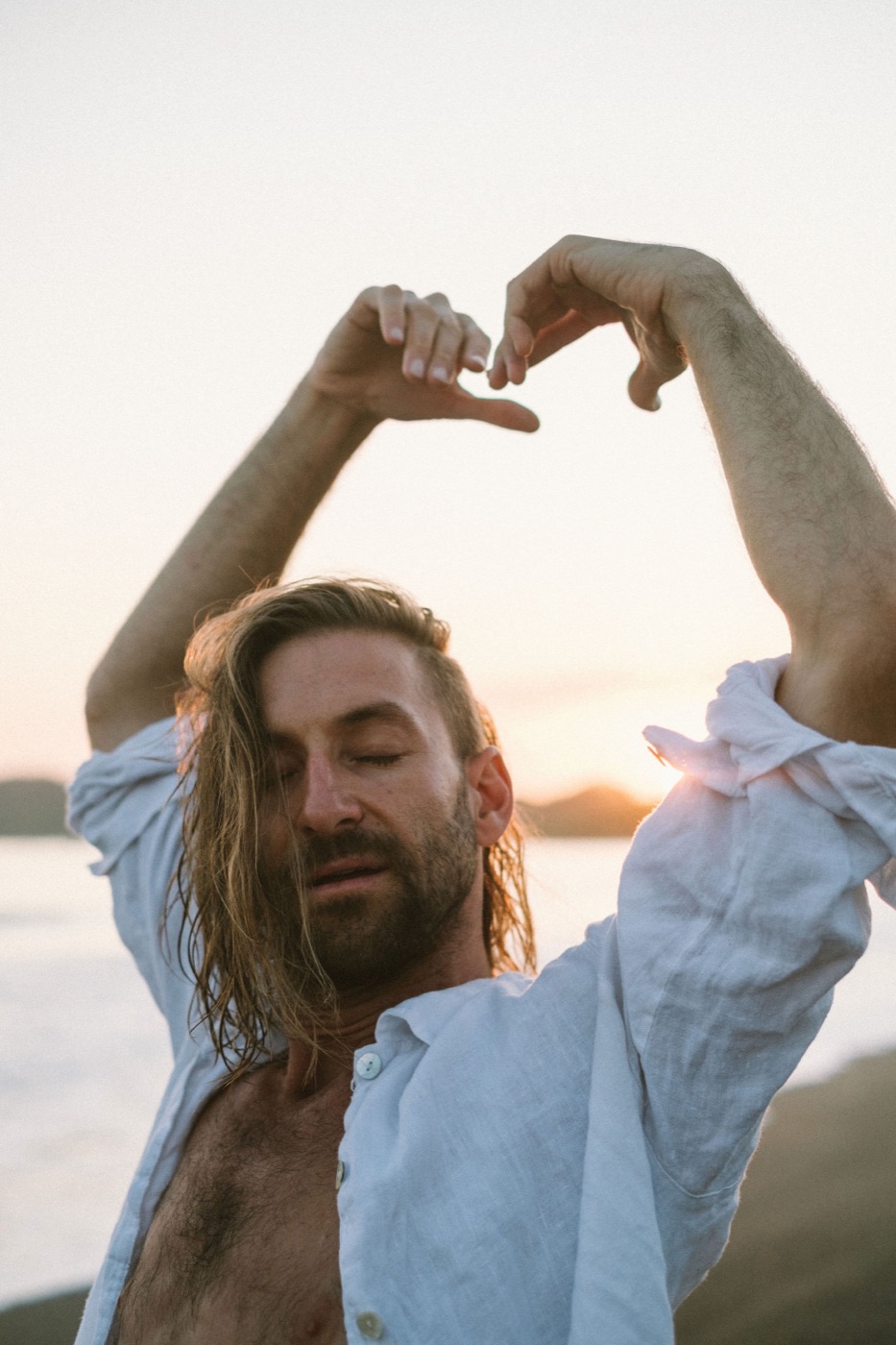 Enrique, the founder, makes a heart with his hands against the sunset sky